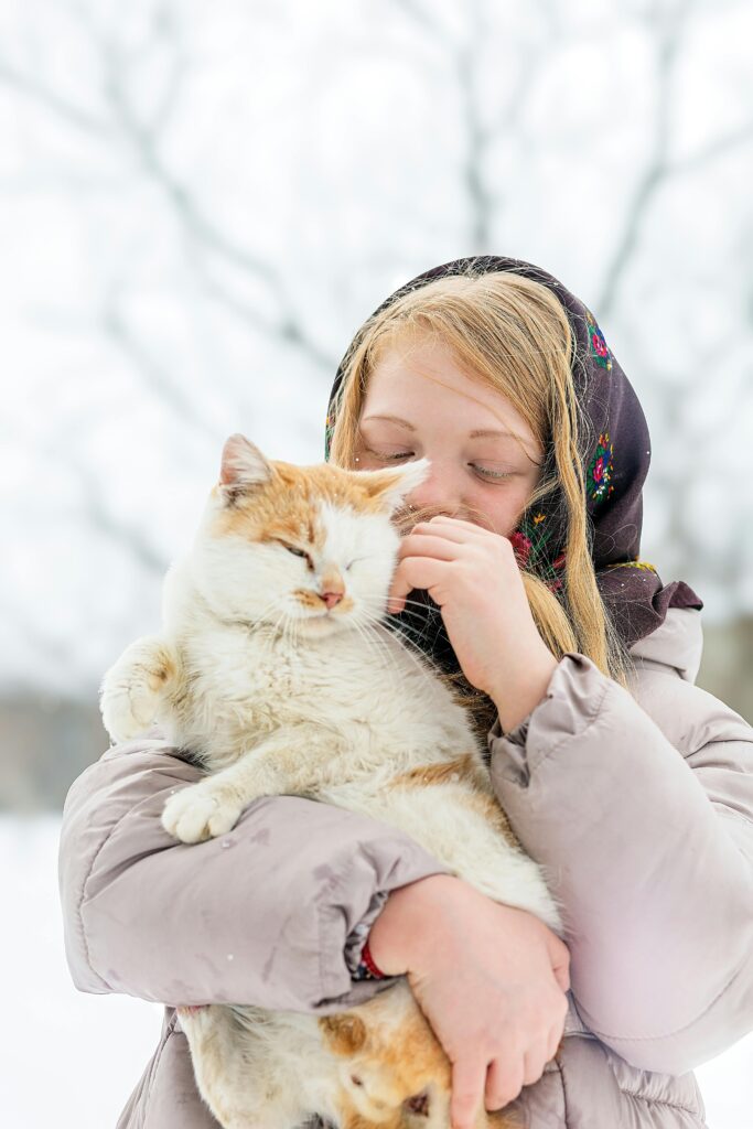 A serene winter portrait of a blonde woman holding a fluffy cat outdoors.